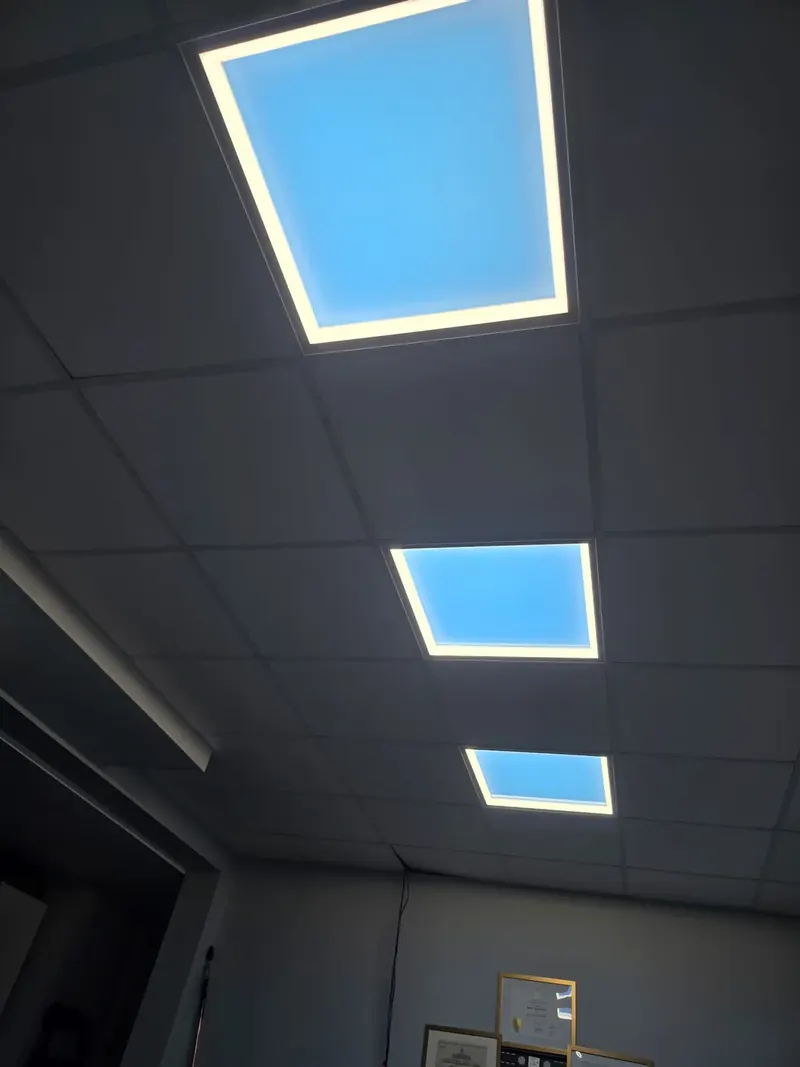 Three LED sky panels in a row in the drop ceiling of a basement with no windows